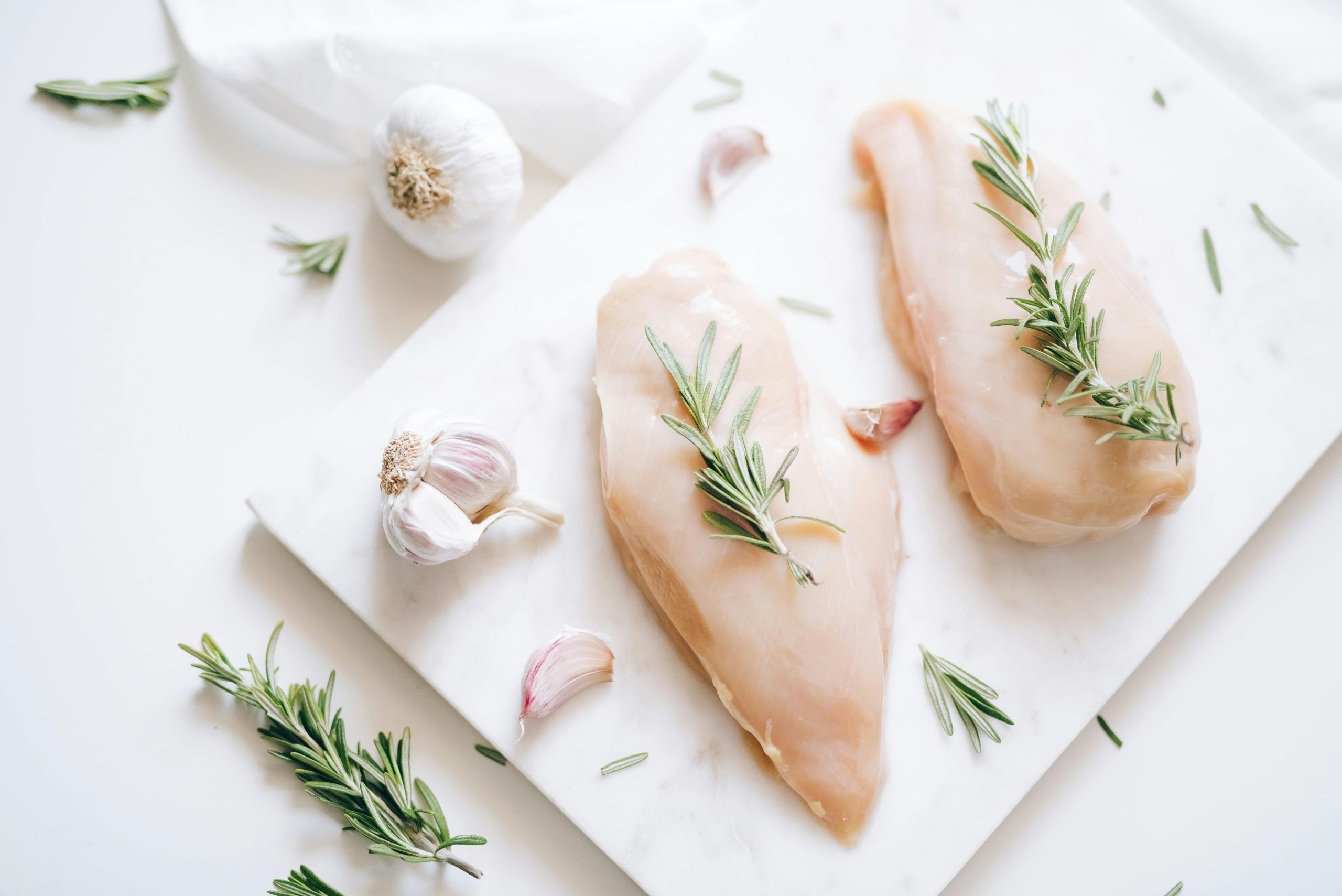 two pieces of raw chicken breast with rosemary sprigs